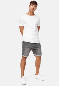T-shirt en coton blanc à manches courtes, associé à un short en denim gris avec des ourlets retroussés. Des baskets blanches complètent le look.