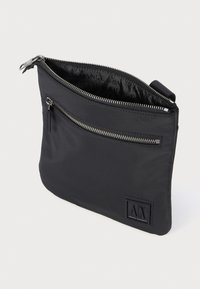 Pochette nera con zip e patch del logo Armani Exchange, tasca frontale con zip e zip superiore parzialmente aperto che mostra la fodera interna con il marchio.