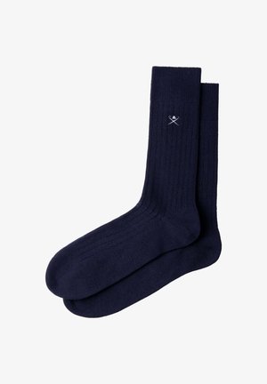 Par de calcetines azul marino acanalados con un pequeño emblema blanco de espadas cruzadas y calavera cerca del puño superior.