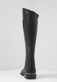 Mustat nahka polvipituiset saappaat, joissa on palotettu rakenne, kultainen yksityiskohta korossa ja vetoketjusulku takana. Pyöreä kärki ja tukevat pohjat.