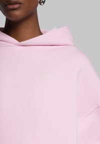 Felpa con cappuccio rosa in tessuto morbido e vestibilità comoda. Presenta un discreto logo bianco "WRSTBHVR" sul petto.