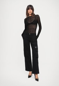 Body in pizzo nero a maniche lunghe con motivo a onde, abbinato a pantaloni cargo neri a gamba larga con tasca con zip. Tacchi a punta neri.