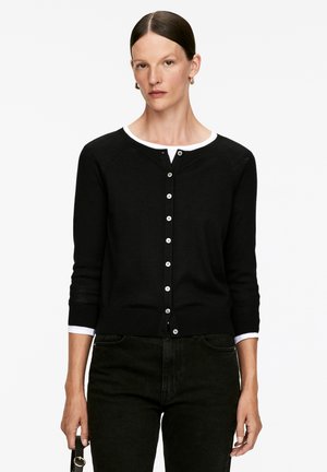 Black cardigan in soft knit, featuring a round neckline, white trim, and button closure. Long sleeves with ribbed cuffs.