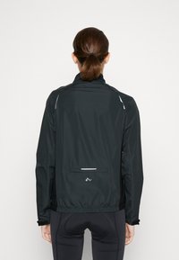 Chaqueta ligera negra con un cuello alto, detalles reflectantes, cintura elástica y bolsillo trasero. Textura suave, diseñada para el uso activo.