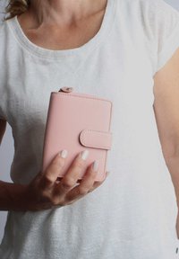 Helle rosa Lederbörse mit Druckknopfverschluss, in einer Hand präsentiert. Verfügt über eine glatte Textur und dezente Steppnähte. Kompaktes Design.