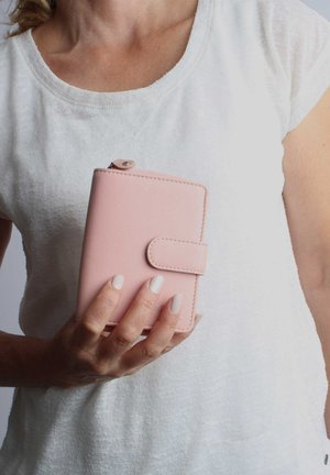 Helle rosa Lederbörse mit Druckknopfverschluss, in einer Hand präsentiert. Verfügt über eine glatte Textur und dezente Steppnähte. Kompaktes Design.