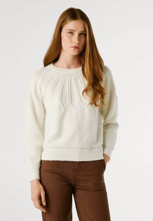 Maglione lavorato a maglia color crema con motivo a diamante testurizzato, polsini e vita a costine, abbinato a pantaloni marroni.