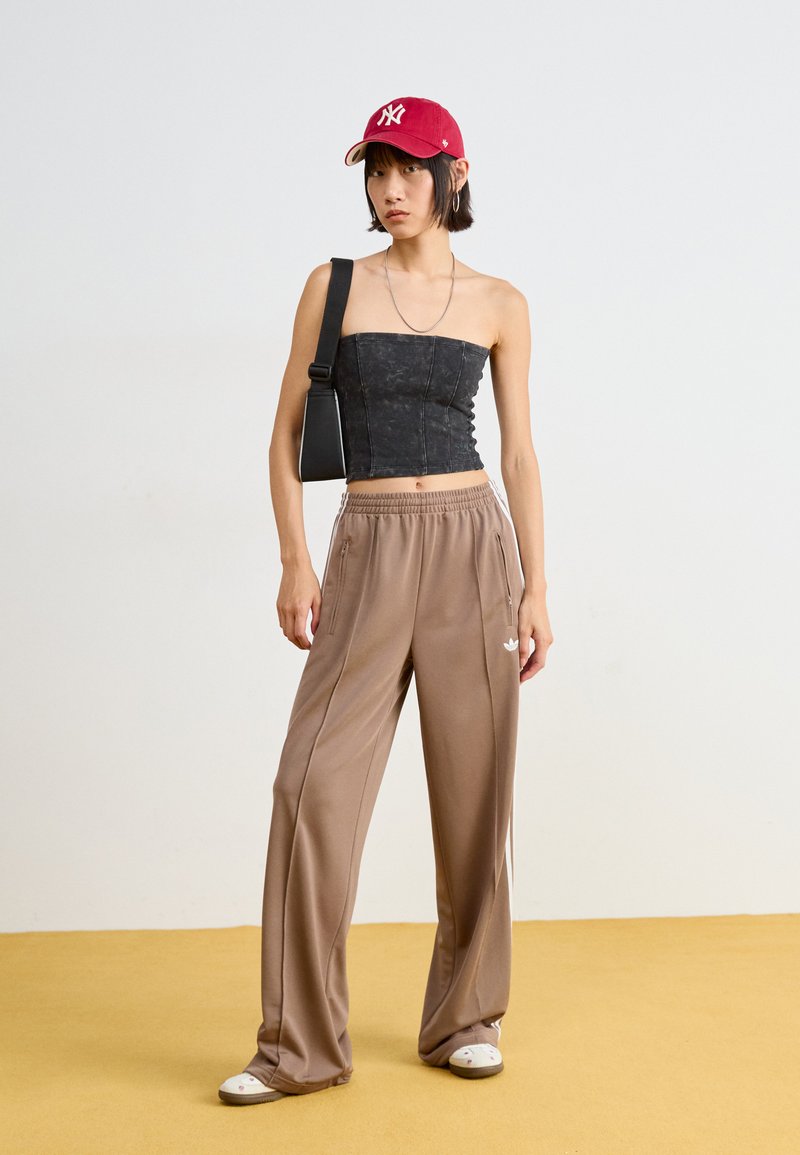 Top nero senza spalline, pantaloni beige chiaro a vestibilità ampia con cerniere laterali, cappellino rosso con logo bianco, collana di argento a più strati, scarpe bianche.