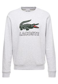 Grå sweatshirt med långa ärmar, med en grön krokodil-logotyp och ordet "LACOSTE" i fet svart text. Mjuk struktur, design med rundad hals.
