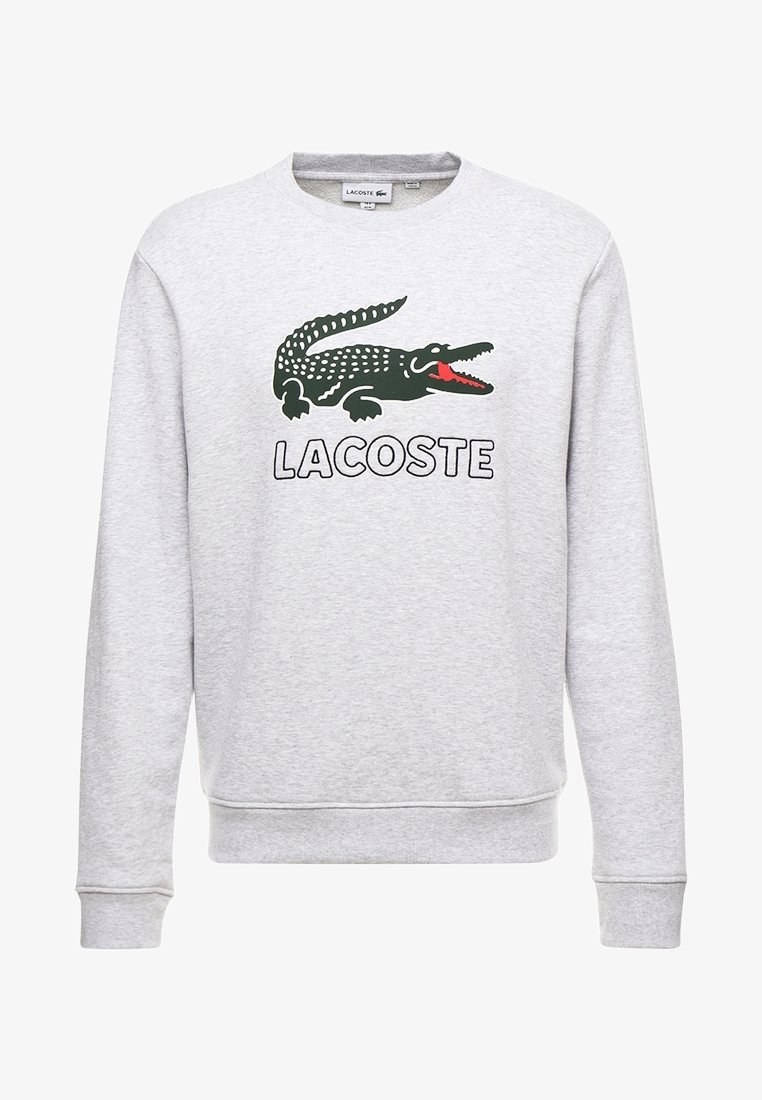 Grå sweatshirt med långa ärmar, med en grön krokodil-logotyp och ordet "LACOSTE" i fet svart text. Mjuk struktur, design med rundad hals.