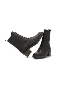 Botas de cuero negras hasta el tobillo con punta redonda y un tacón grueso. Un par presenta cordones, mientras que el otro tiene costuras decorativas.