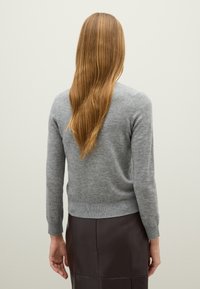 Grijze wollen trui met een ronde halslijn, lange mouwen en een geribbelde zoom, gecombineerd met een donkere leren rok. Gladde textuur en aansluitend ontwerp.