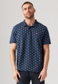 Cămașă polo bleu marin cu guler, având un model alb repetat. Mâneci scurte și un mic logo roșu Levi's pe piept.