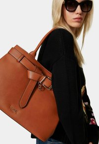 Brun læder tote taske med en struktureret design, der har en spændeaccent og robuste håndtag. Teksturér overflade med en poleret finish.