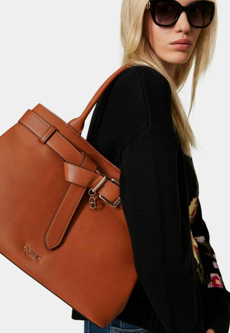Braune Leder-Tote mit einem strukturierten Design, ausgestattet mit einer Schnallenakzentuierung und stabilen Griffen. Strukturierte Oberfläche mit glänzender Verarbeitung.