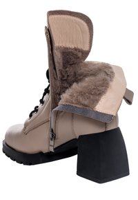 Stivale beige con lacci e cerniera, fodera in pelliccia sintetica e tacco spesso nero. Presenta un design ripiegato e dettagli in suede.