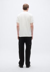 Valge lühikeste varrukatega T-särk ümarkaelusega, millele on kombineeritud lahtised mustad cargo-püksid, millel on küljetaskud ja trukknööbid.