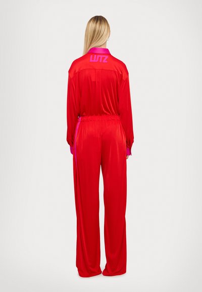 Combinaison en satin rouge avec manches longues, col et taille élastique. Présente des accents roses contrastants sur le col et les poignets. Le dos affiche « WTZ ». 