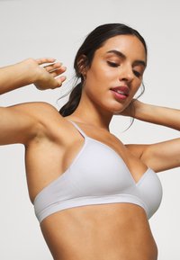 Lichtgrijze driehoekige bralette gemaakt van glad materiaal met dunne bandjes en een naadloos ontwerp, met een subtiele glans en zonder versieringen.
