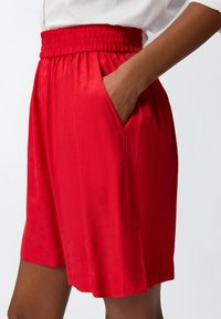 Pantaloni rossi realizzati in tessuto liscio, dotati di una cintura elastica, tasche laterali e una vestibilità comoda con una leggera texture.