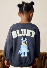 Navy Sweatshirt mit großem "BLUEY"-Schriftzug in Creme und einer Grafik des Charakters Bluey auf der Rückseite. Mit Rippbündchen und Saum.