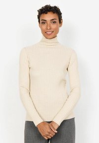 Beige ribbed turtleneck sweater with long sleeves, fitted design, and a soft texture, paired with gray vertical striped pants.