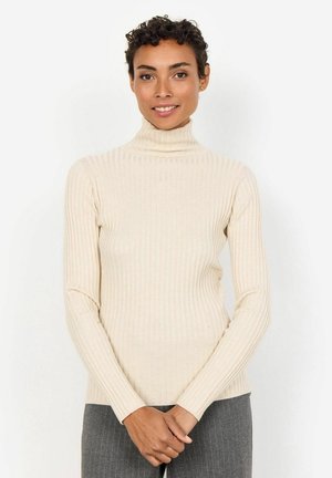 Maglione a collo alto beige a coste con maniche lunghe, design aderente e una consistenza morbida, abbinato a pantaloni grigi a righe verticali.