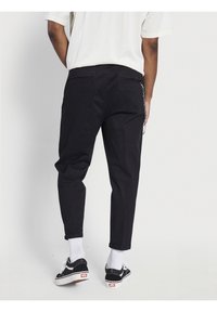 Pantaloni di cotone neri con una vestibilità rilassata, dotati di tasche laterali e di un dettaglio a catena sulla tasca posteriore. Orli con risvolto, abbinati a sneaker nere.
