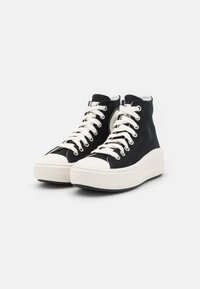 Czarne sneakersy na wysokiej podeszwie wykonane z płótna z białymi gumowymi podeszwami i czubkami. Posiadają białe sznurówki oraz etykietę z logo po zewnętrznej stronie.