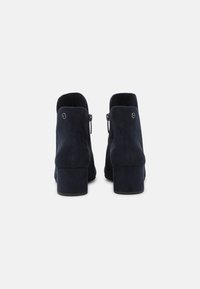 Marineblaue Wildleder-Ankle Boots mit einem Blockabsatz, Reißverschluss und minimalistischer Gestaltung sowie einem dezenten Logo-Detail auf der Rückseite.