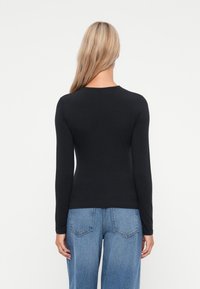 Sort langærmet top med rund halsudskæring, tætsiddende design og glat tekstur, båret med lyseblå højtaljede jeans.