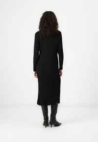 Black ribbed knit dress with long sleeves, mid-calf length, and side slits, paired with black fitted heeled boots.