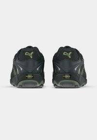 Baskets noires de sport avec une tige en mesh, des accents verts et un soutien de talon texturé. Présente le logo "CELL" à l'arrière.