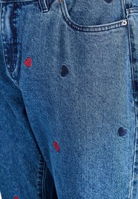 Denim jeans met een medium was hebben geborduurde harten in rood en donkerblauw, wat textuur en visuele interesse aan de stof toevoegt.