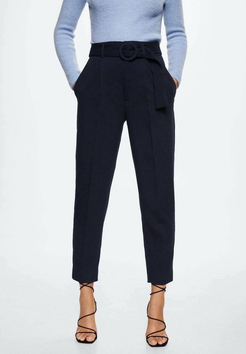 Femme portant un pantalon noir taille haute fuselé avec une ceinture en tissu, un pull bleu clair et des sandales noires à talons hauts et à brides.