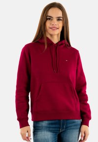 Sudadera con capucha color burdeos con bolsillo frontal tipo canguro, puños y dobladillo acanalados, y un pequeño detalle de logo en el pecho. Textura de material suave.