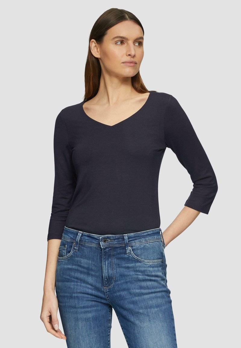 Marineblauw sportshirt met lange mouwen en V-hals, gemaakt van zachte stof. Gecombineerd met blauwe jeans met een klassieke pasvorm en standaard zakken.