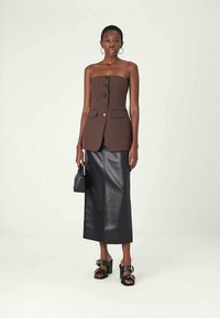 Brown strapless top with button detailing, paired with a black leather maxi skirt. Model wears black platform sandals and holds a small bag.