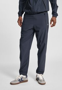 Marineblauwe sportbroek met een relaxte pasvorm, voorzien van witte biezen en zijzakken. Gecombineerd met grijze en marineblauwe sneakers.