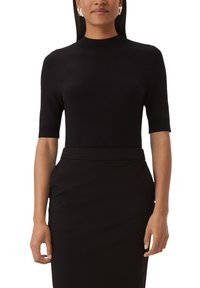 Haut en maille noir à manches courtes avec un col haut. Texture lisse avec une silhouette ajustée, associé à une jupe crayon noire.