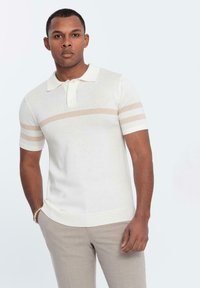 Kortärmad pikétröja i krämfärgad med två beige horisontella ränder på ärmarna. Tillverkad av ett mjukt tyg, med en krage och knäppning framtill.