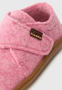 Chausson en feutre rose avec une forme courbée, des coutures piquées et une étiquette logo marron. La semelle est beige et conçue pour un usage intérieur.