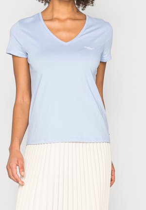 Hellblaues Baumwoll-T-Shirt mit V-Ausschnitt, kurzen Ärmeln und einem kleinen, gestickten Logo auf der linken Brust. Glatte, weiche Textur.