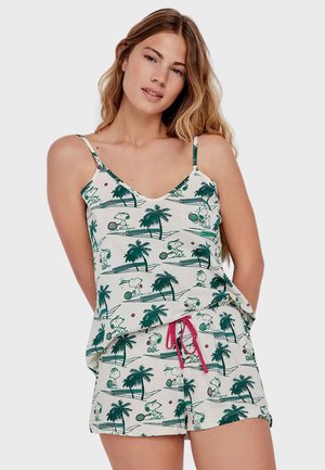 Femme portant un caraco blanc et un short avec un motif de palmier vert et Snoopy jouant au tennis, avec un cordon rose sur le short.