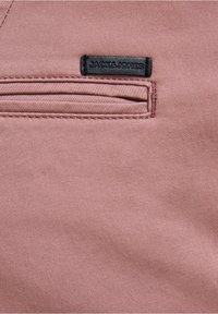 Różowy materiał o lekko teksturowanej powierzchni, z czarną metką z napisem "JACK&JONES" oraz małą poziomą kieszonką na zamek.