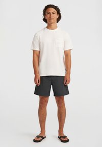 T-shirt blanc à texture, à manches courtes, avec une poche sur la poitrine, associé à un short de bain noir et des tongs noires. Tenue de plage simple et décontractée.