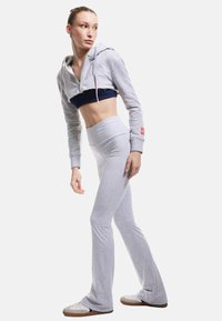 Grijze cropped hoodie met een rits, gecombineerd met hoog getailleerde grijze flared leggings. Geweven stof, casual ontwerp. Lichtbruine sneakers.