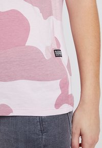 Růžové tričko s krátkým rukávem v maskáčovém vzoru vyrobené z měkké tkaniny. Na lemu má štítek G-Star. Hladká textura s nepravidelnými, zaoblenými vzory.