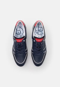 Navy leather sneakers with white accents, perforated design, and red collar. Laces are navy; insoles feature a blue and white pattern.