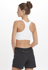 Hvid sportsbh med racerback-design, parret med sorte shorts med en bred elastisk talje og kontrasterende teksturerede paneler.